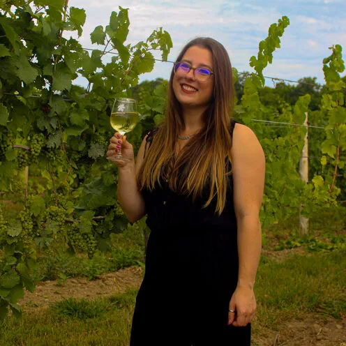 Brooke holding a glass of wine and smiling in the vineyard